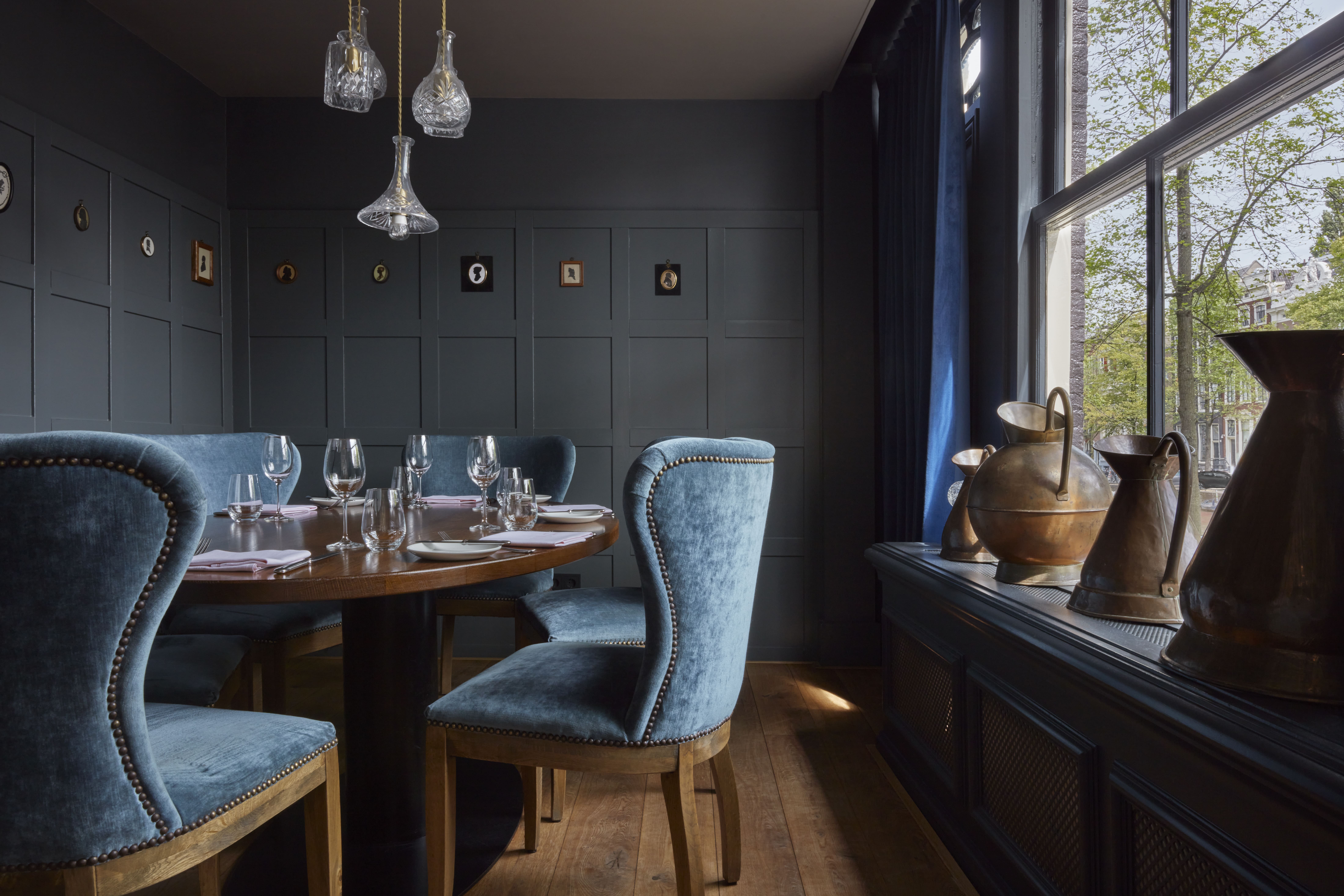 A semi-private dining room at Jansz. Amsterdam with a round table, blue velvet chairs, and pendant lights.