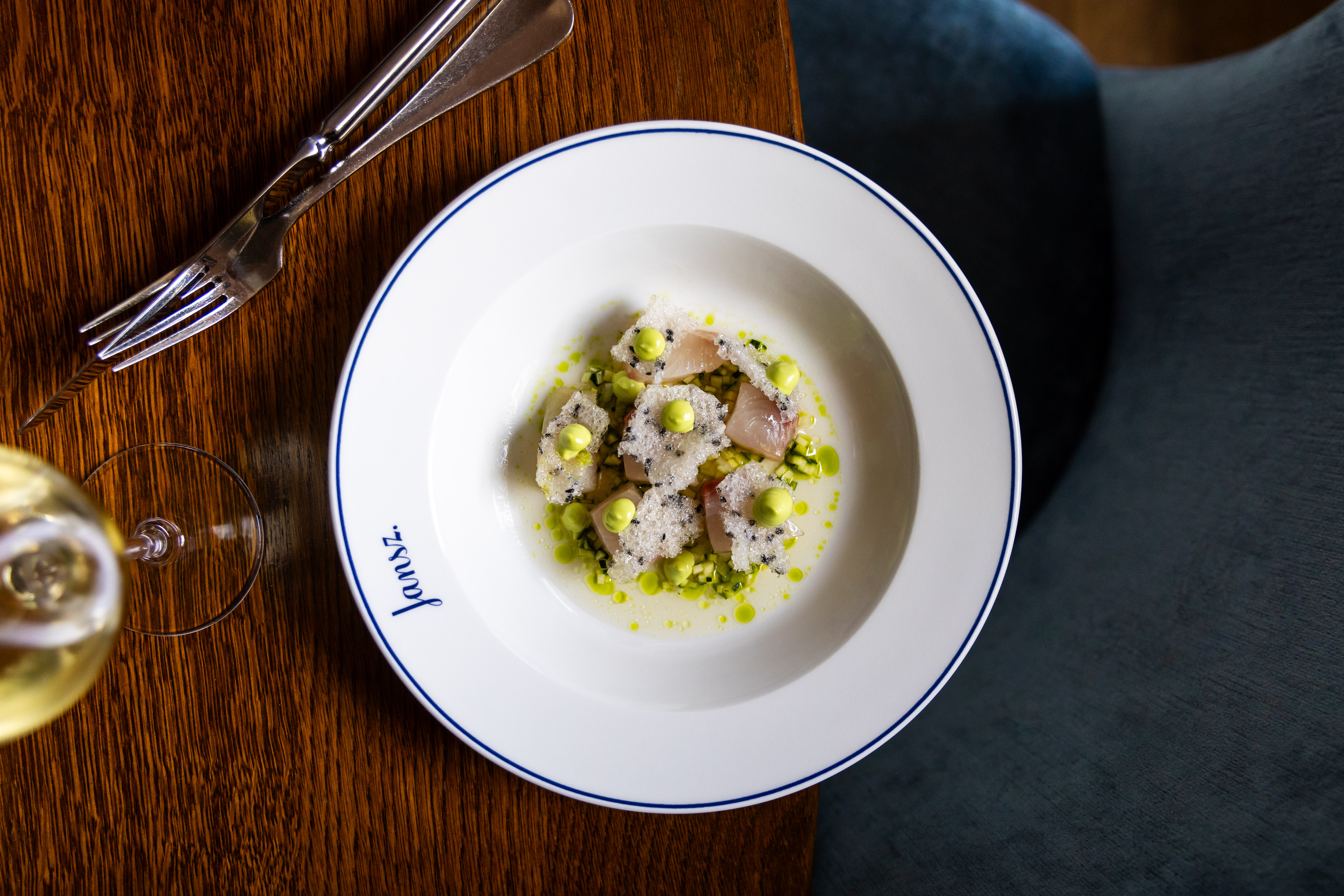 A vibrant dish of sliced fish with green sauce, garnished with small dollops of avocado and sprinkled with salt at Jansz.