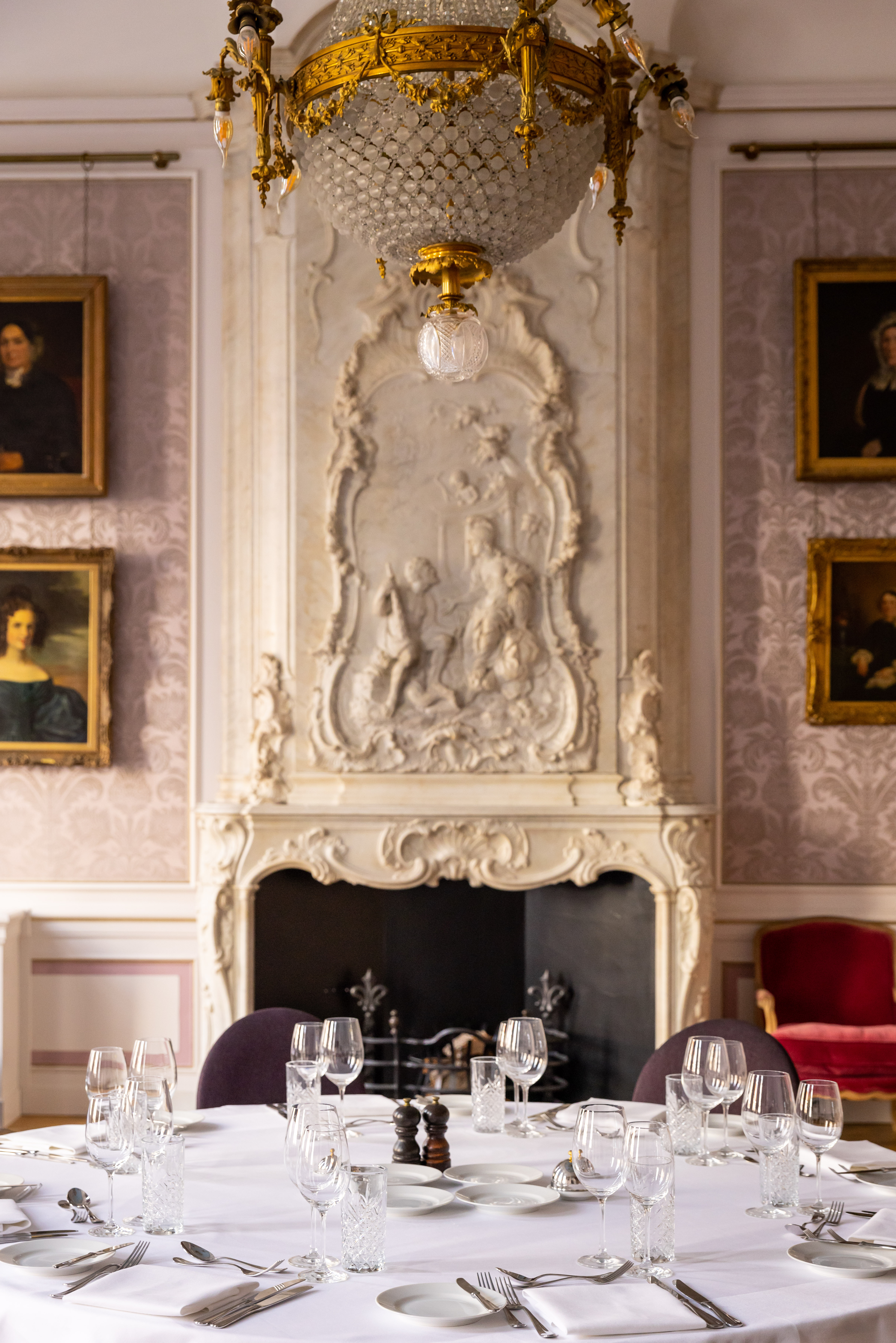 A formal dining table at a banquet at Pulitzer Amsterdam with crystal glassware and silver cutlery, with a marble fireplace.