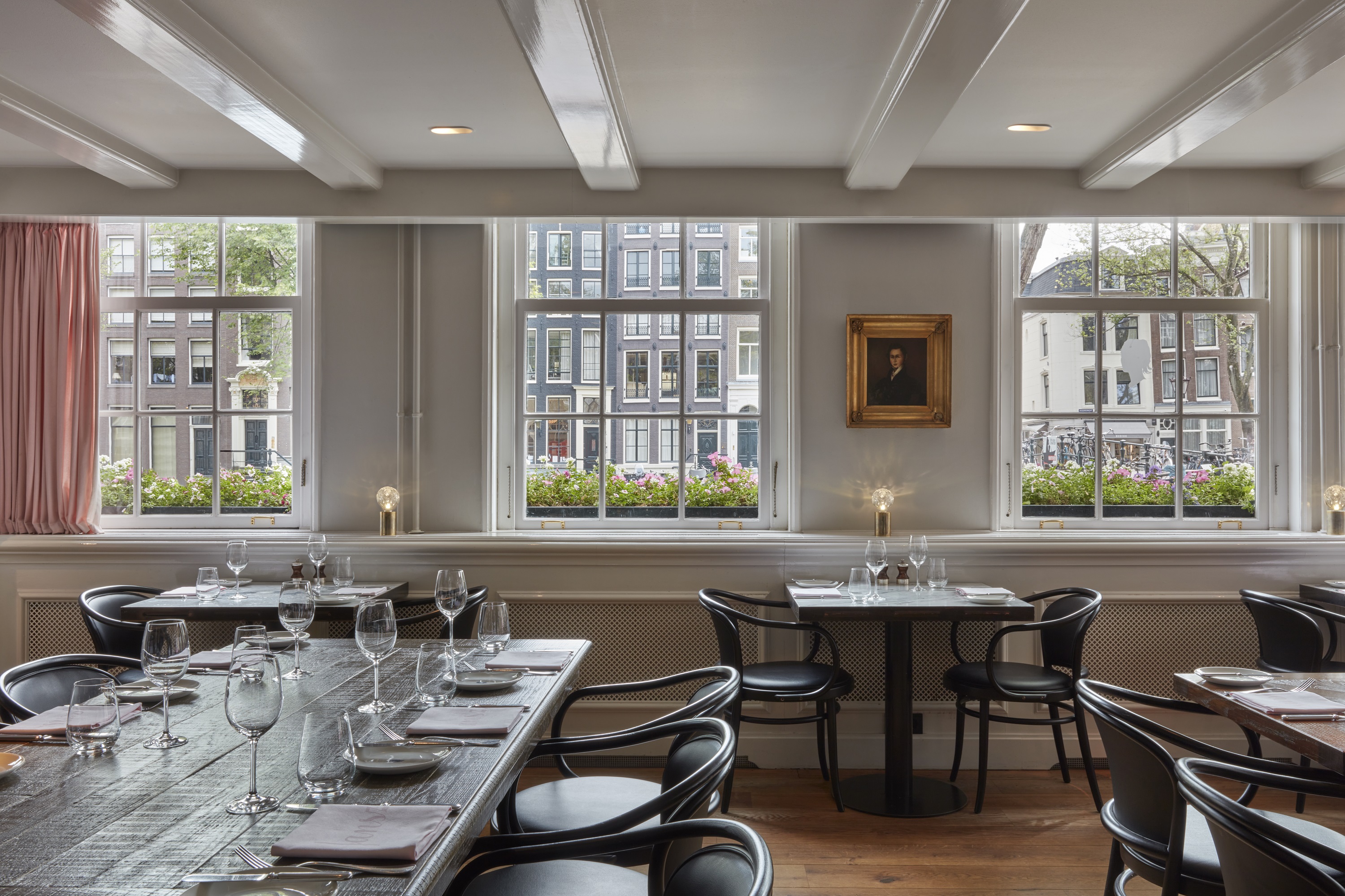 Light and stylish Jansz. restaurant with black chairs and tables set near large windows with views of the Amsterdam street.