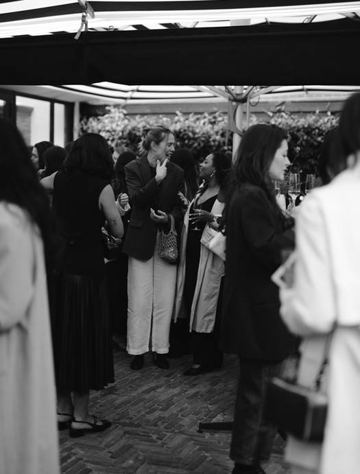 A black-and-white photo of a small crowd enjoying drinks and conversation at a gathering in the garden of Jansz. restaurant.